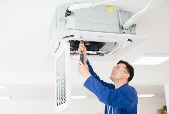 Maintenance et réparation de climatisation cassette CVC. Technicien CVC en bleu et lunettes de sécurité réparant une unité de climatisation cassette fixée au plafond. Maintenance professionnelle.